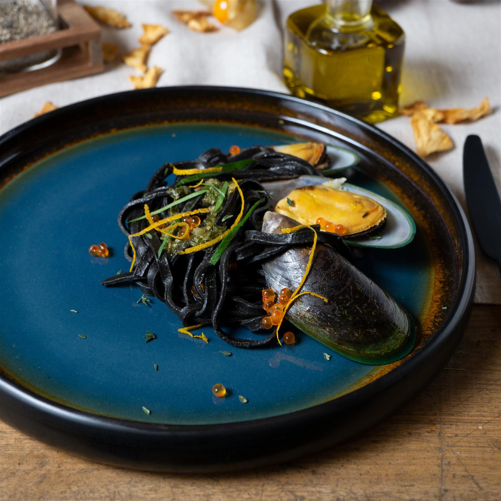 Modernes Geschirrset in Grün und Blau – 12-teiliges Tellerset aus Keramik für stilvolles Essen Geschirrset in Grün und Blau, bestehend aus Tellern, Schüsseln und Tassen, ansprechend auf einem Holztisch arrangiert, mit Besteck und Servietten, vor neutralem Hintergrund.