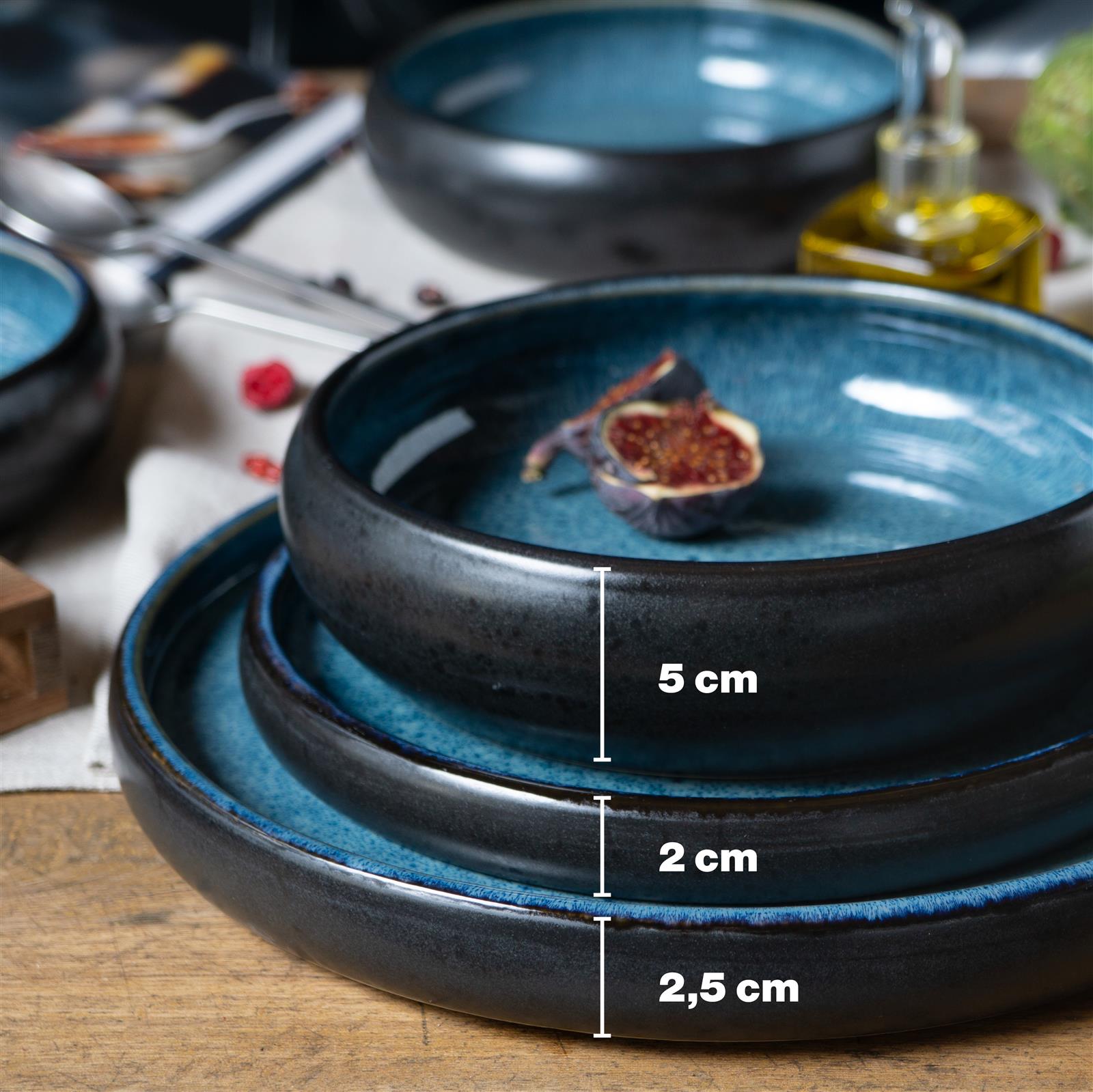 Blaues 16-teiliges Geschirrset aus Keramik bestehend aus vier Speisetellern, vier Desserttellern, vier Schüsseln und vier Tassen, schlichtes Design mit leicht gewellten Rändern, auf weißem Hintergrund arrangiert.