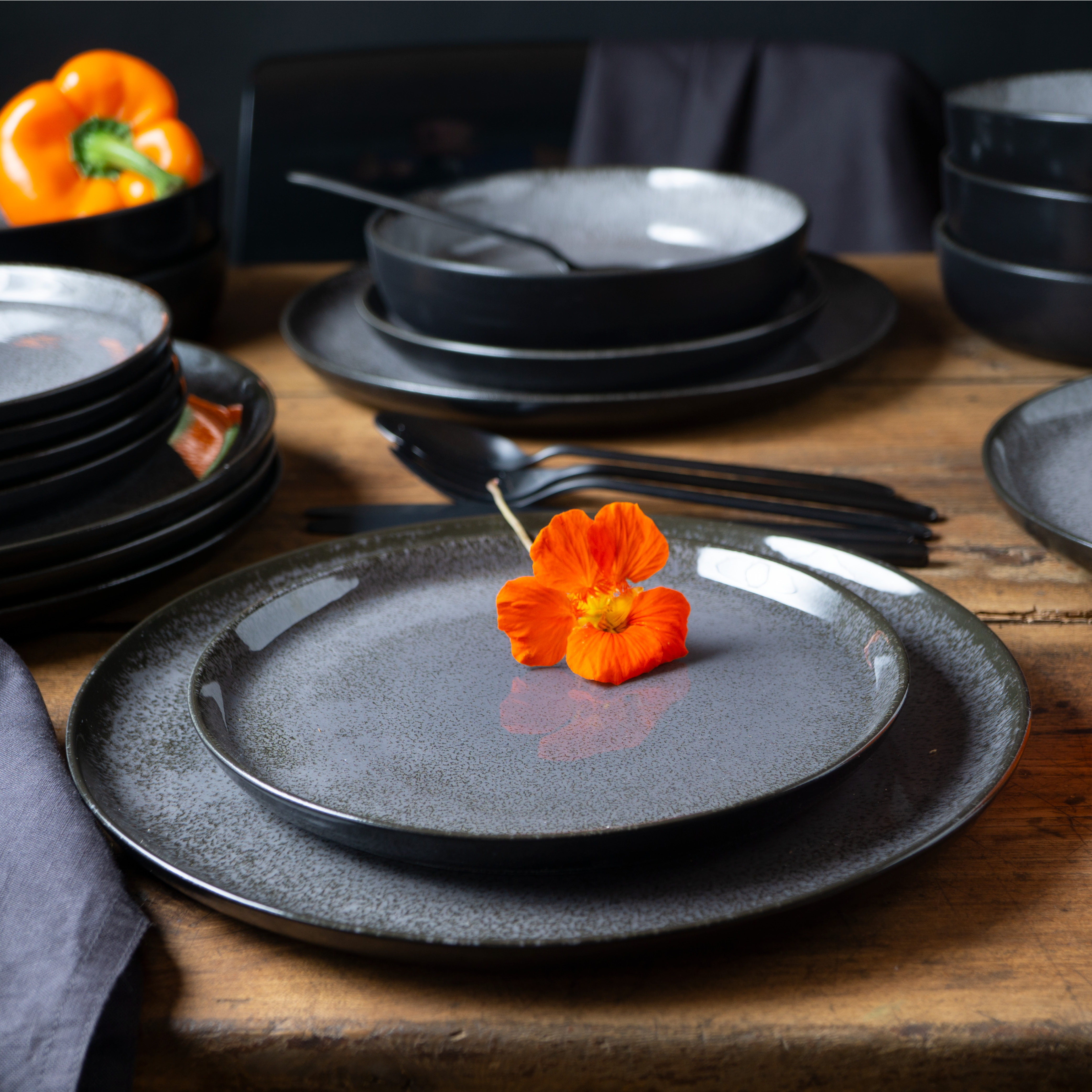 18-teiliges Gourmet-Teller-Set in Anthrazit auf hellem Holztisch arrangiert; bestehend aus flachen und tiefen Tellern sowie Schalen in modernem, mattem Design – ideal für stilvolles Anrichten von Speisen.